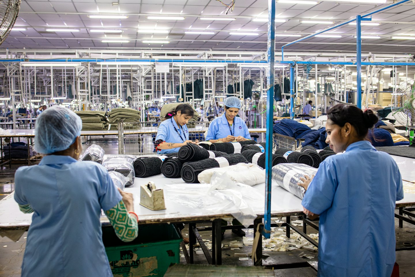 Three women in blue uniforms pack textile rolls in a factory.