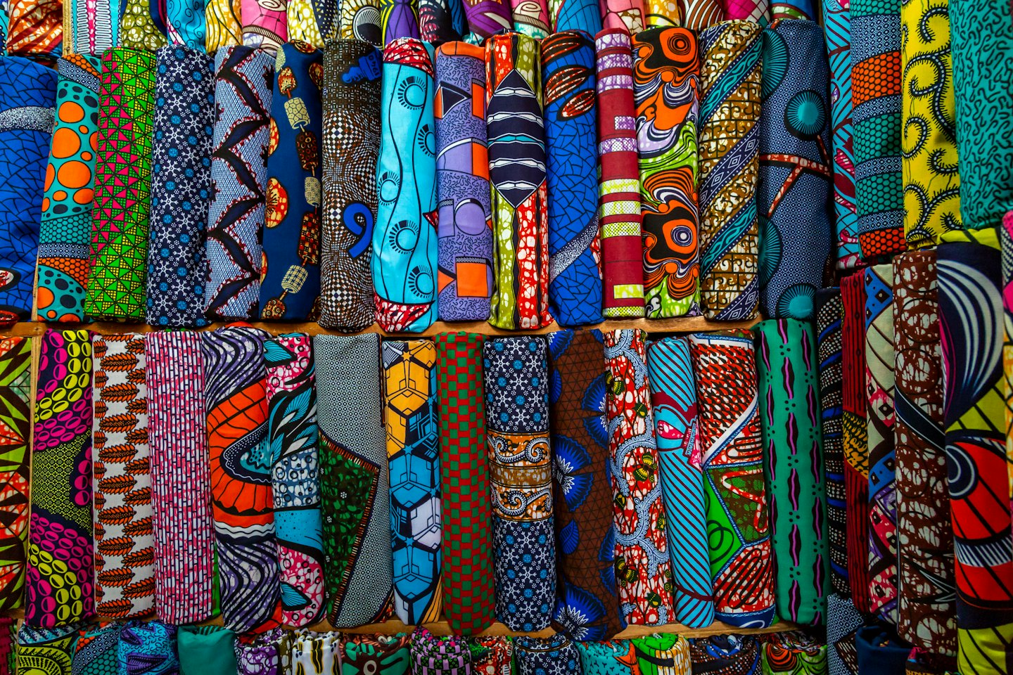 Stacks of colorful, patterned fabric rolls on wooden shelves.