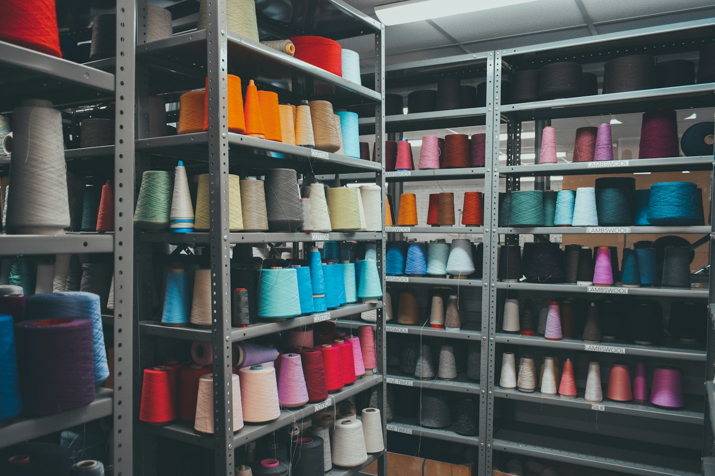 Colorful yarn spools organized on industrial metal warehouse shelves.