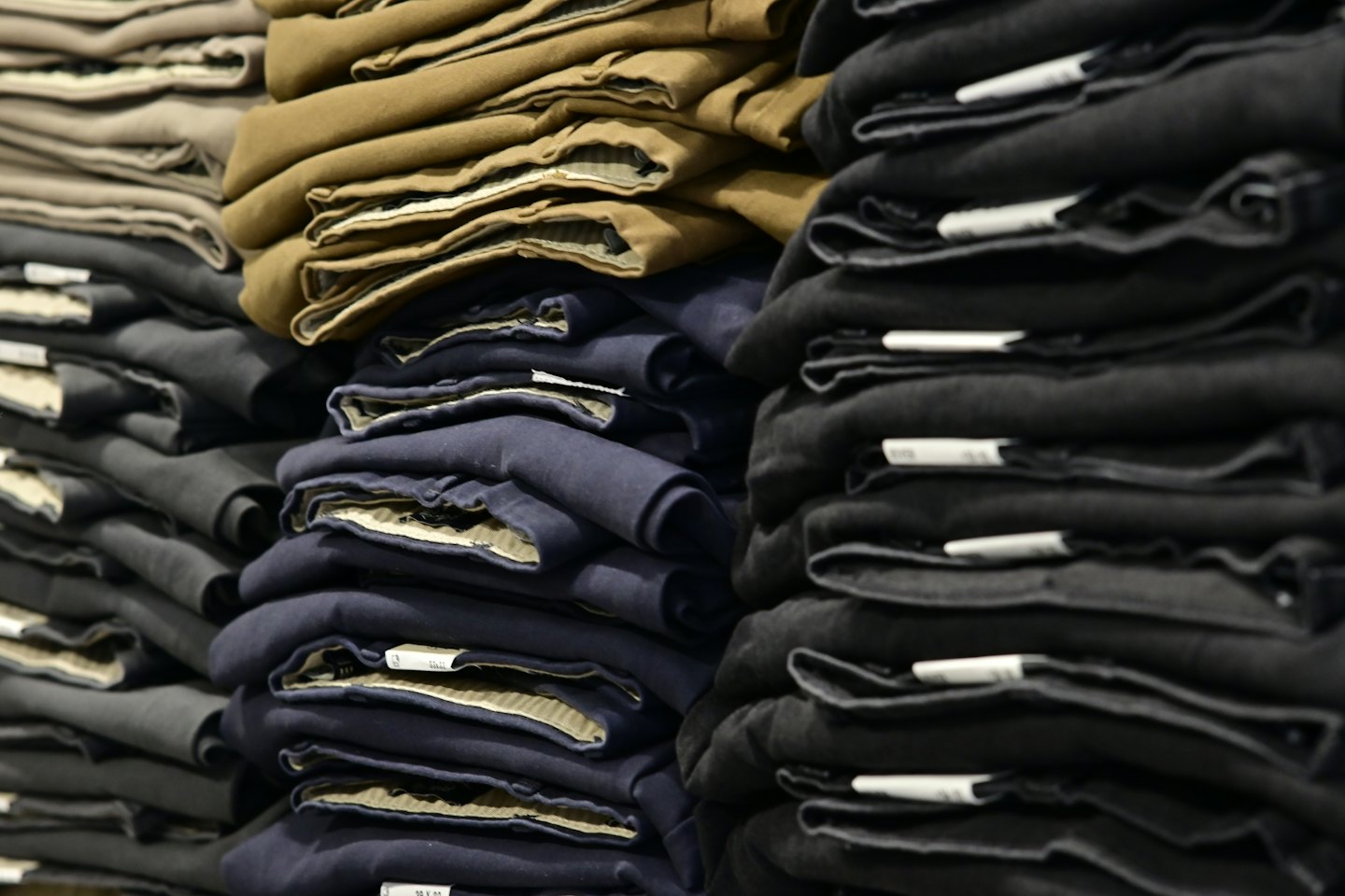 Neatly folded stacks of trousers organized by colour on shelves.