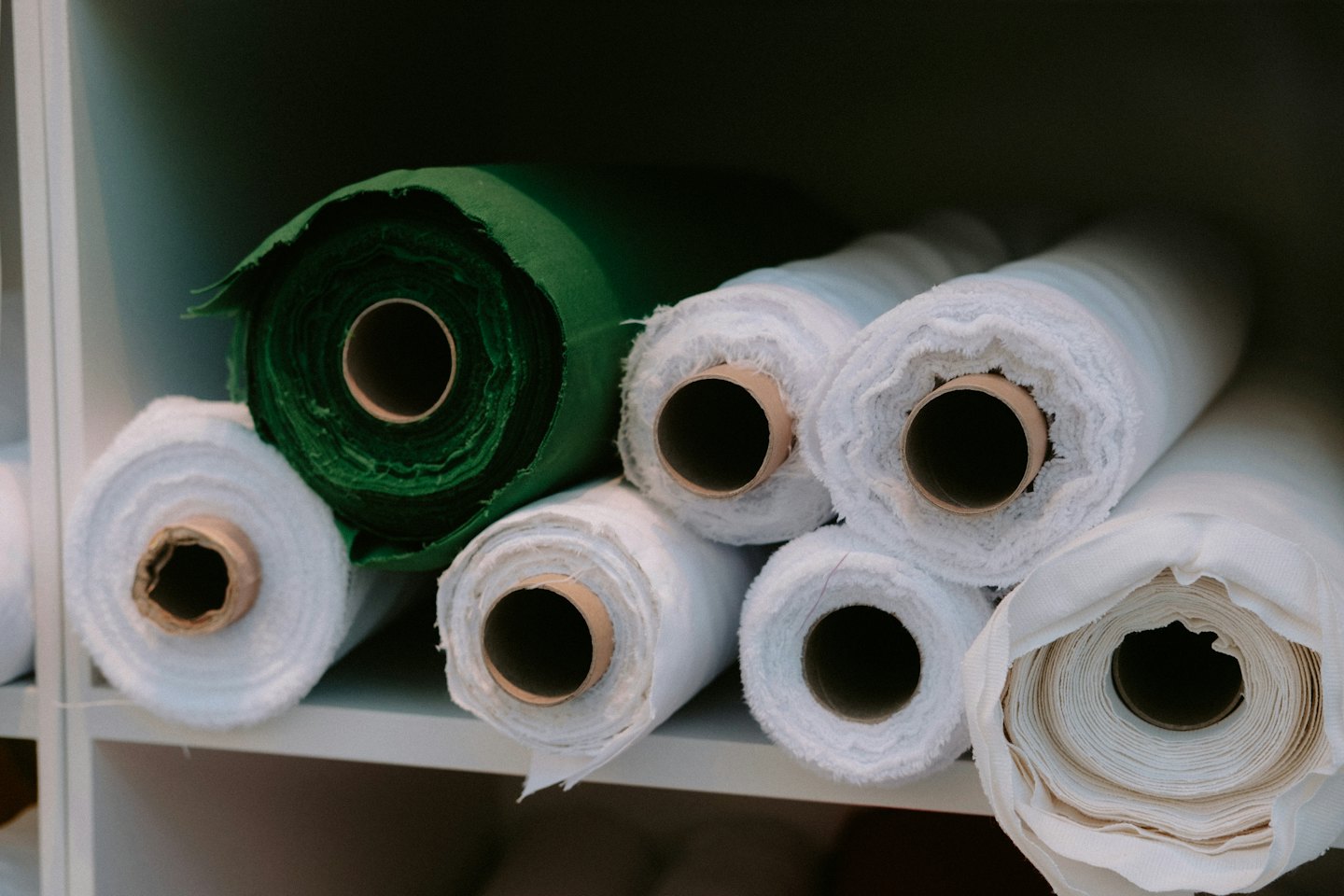 Dark green and white fabric rolls stacked on shelves.