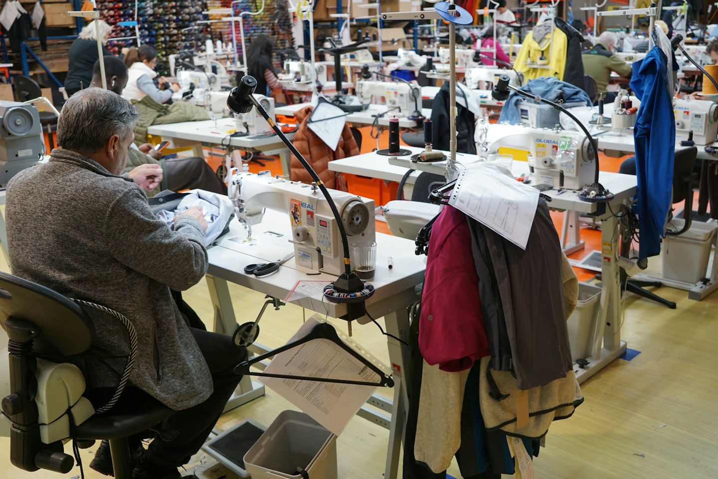 A man in a grey sweater sews fabric at a factory machine.